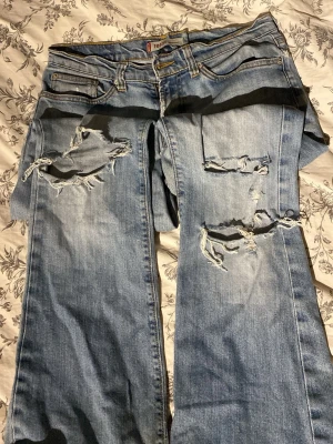 Ljusblå ripped jeans från Topshop - Säljer ett par ljusblå jeans från Topshop med snygga slitningar och hål på benen. Jeansen har klassisk femficksdesign, normal midja och raka ben. Perfekta för en avslappnad och trendig look.