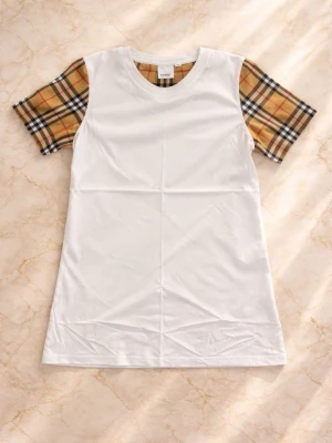 Burrbery tshirt - Snygg vit t-shirt med klassiska beige-rutiga ärmar i brunt, svart och rött. Rak passform och rund halsringning. Perfekt för dig som gillar en stilren look med en twist. Materialet känns mjukt och bekvämt mot huden.