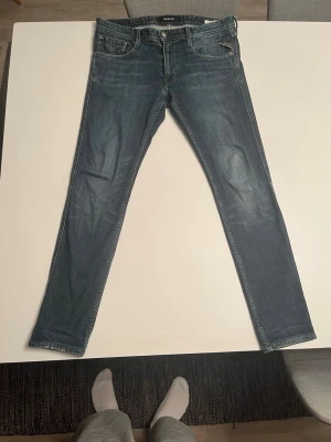 Blå slim fit jeans från Replay - Snygga blå slim fit jeans från Replay med klassisk femficksdesign och diskreta slitningar framtill. Jeansen har normal midja och smala ben, perfekt för en trendig och avslappnad stil. Tillverkade i mjuk denim med stretch för extra komfort. W32 L32