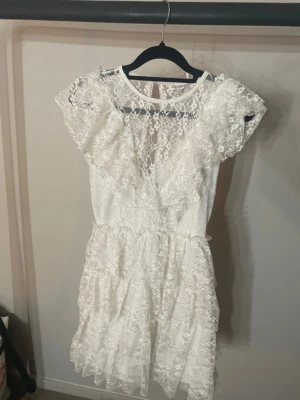 Vit spetsklänning från Bubbleroom XS - VID SNABB FÖRSÄLJNING 500kr! Superfin vit kort spetsklänning från Bubbleroom med volangdetaljer och rund hals. Klänningen har korta ärmar och vackra spetsmönster över hela plagget. Perfekt för sommarens alla tillfällen!