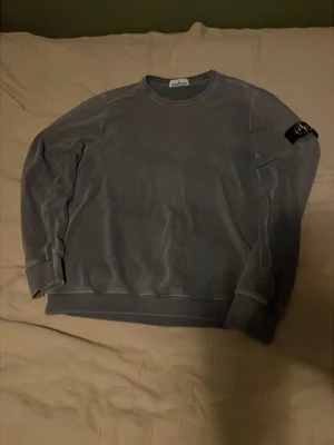  sweatshirt från Stone Island - Snygg grå sweatshirt från Stone Island med klassisk rund hals och ikonisk logotyp-patch på vänster ärm. Tröjan har ribbade muddar vid ärmslut och nederkant. Perfekt för en avslappnad och stilren look.