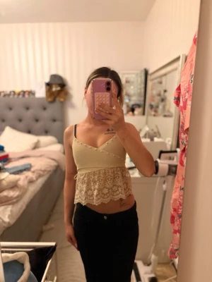 Beige croppad spetslinnetopp - Säljer en beige croppad linnetopp med spetsdetaljer nedtill. Toppen är ärmlös och har en v-ringad form med tunna axelband. Perfekt för dig som gillar en feminin och trendig stil.