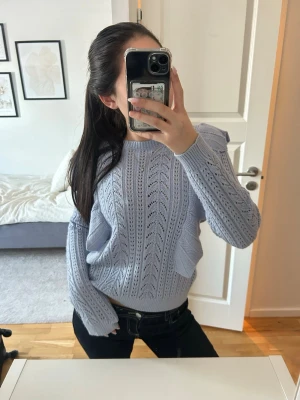 Ljusblå stickad tröja med volang - Ljusblå stickad tröja med dekorativt hålmönster och volangdetaljer längs ärmarna. (På tröjans baksida har en söm gått upp, bild 3) Så fin färg och jätteskön 💙✨💞✨🤞🫶den är större i storleken och passar xs-m 