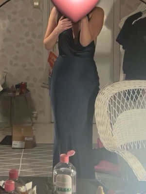 Mörkblå långklänning i satin - Säljer en elegant mörkblå långklänning med smala axelband och v-ringad hals. Klänningen har en figurnära passform och är tillverkad i glansigt satinmaterial som ger en lyxig känsla. Perfekt för dig som vill sticka ut på nästa bal eller fest.