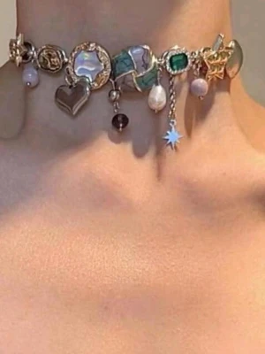 Choker med färgglada berlocker - Unikt chokerhalsband med mixade berlocker i guld- och silverfärg, pärlor, stjärnor, hjärta, ko och stenar i grönt, lila och turkost. Halsbandet har en lekfull och trendig design med detaljer i metall, emalj och glas. Perfekt för dig som vill sticka ut med accessoarer.