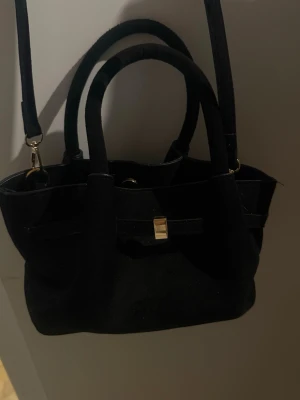 Svart handväska med gulddetalj - Stilren svart handväska i tyg med två handtag och avtagbar axelrem. 