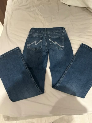 Lågmidjade jeans från Nelly - Säljer ett par blå bootcut jeans med snygga broderade detaljer på bakfickorna. Använda några gånger men inga skavanker, säljer då dom blivit förstora. 