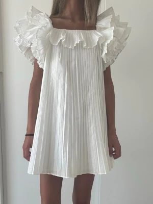 Vit plisserad klänning med volang - Sååå sjukt fin och populär klänning från Zara! I storlek M 💓💓 extremt eftertraktad och så fin till student eller liknande! Bilderna är mina egna