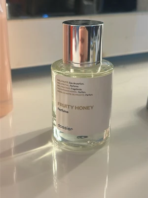 Fruity Honey parfym från Dossier - En stilren parfymflaska från Dossier med doften Fruity Honey. Flaskan är genomskinlig med en vit etikett och har ett snyggt silverfärgat lock. Perfekt för dig som gillar fruktiga och söta dofter.