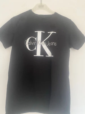 Svart Calvin Klein Jeans t-shirt - Svart t-shirt från Calvin Klein Jeans med stort vitt CK-tryck och logga framtill. Klassisk rund hals och korta ärmar. Perfekt basic-plagg med snygg streetkänsla. Tillverkad i mjuk bomull för skön komfort.
