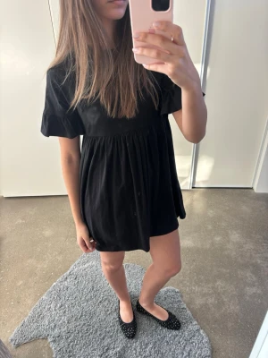 Svart kort klänning  - En svart kort klänning med rund hals och korta puffärmar. Passar dig med storlek S/M