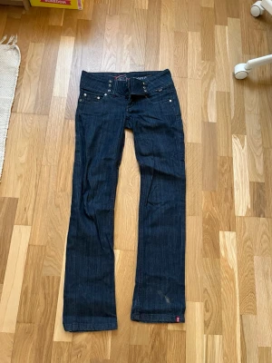 Mörkblå bootcut jeans från cdc by esprit - Snygga mörkblå bootcut jeans med flera silverfärgade knappar i midjan. Jeansen har en låg midja och lite utsvängda ben. 