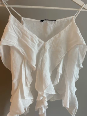Vit volangtopp Zara - Säljer en vit volangtopp med smala axelband och v-ringad front. Toppen har flera lager av volanger som ger ett luftigt och romantiskt uttryck🤍I storlek S men passar Xs lika bra!