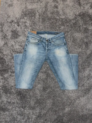 Ljusblå jeans från Dondup - Säljer ett par ljusblå jeans från Dondup med snyggt slitna detaljer och klassisk femficksmodell. Jeansen har dragkedjor på bakfickorna och en avslappnad passform. Perfekta för dig som gillar en trendig och avslappnad stil.