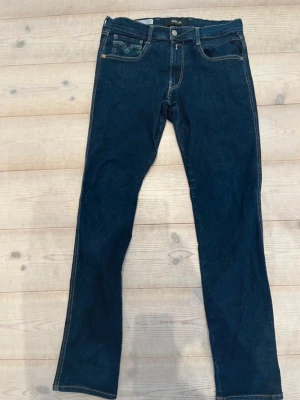 Mörkblå jeans från Replay - Snygga mörkblå jeans från Replay med klassisk femficksdesign och raka ben. Jeansen har kontrastsömmar och detaljerade bakfickor med broderi. Perfekta för en stilren och avslappnad look.