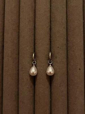 Silverörhängen med droppformade pärlor - Snygga örhängen i silverfärg med droppformade vita pärlor som hänger från små ringar. Perfekta för dig som gillar stilrena och eleganta accessoarer. Passar till många olika looks och är lätta att bära hela dagen.