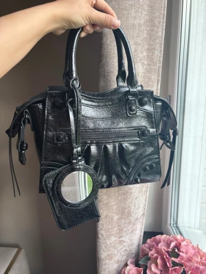 Svart handväska från Steeve Madde - Cool svart handväska i glansigt konstläder från Steeve Madden, medföljer en matchande liten spegel i fodral som hänger på väskan samt ett band man kan sätta på och av. Verkligen perfekta skolväskan💗.
