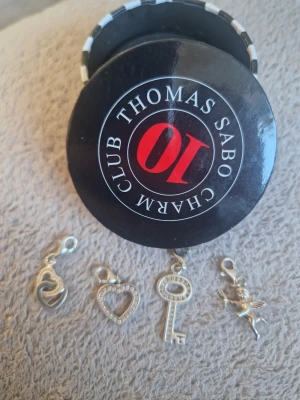 Thomas Sabo silverberlocker 4-pack - Fyra snygga berlocker från Thomas Sabo i silverfärg. Setet innehåller ett hjärta, ett hjärta med stenar, en nyckel och en älva. Perfekta att hänga på armband eller halsband. Kommer i original ask.