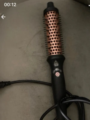 Rundborste med värme, svart/koppar - Elektrisk rundborste i svart och kopparfärg med borstpiggar och värmefunktion. Perfekt för att styla och forma håret. Har en av/på-knapp och sladdanslutning. Cylindrisk form och greppvänligt handtag.