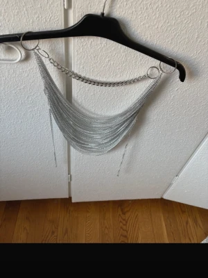 Statement halsband i silverfärgade kedjor - Säljer ett riktigt coolt statement halsband i silverfärg. Halsbandet består av flera lager tunna kedjor som hänger i en bågform mellan två stora ringar. Perfekt för att lyfta vilken outfit som helst med en edgy vibe.