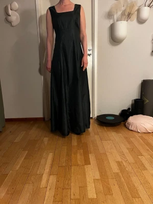 Klänning - Elegant svart långklänning med breda axelband och fyrkantig ringning. Klänningen passar perfekt till speciella tillfällen som bal, bröllop och fester.