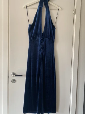 Mörkblå sammetsklänning med halterneck - Supersnygg långklänning i mörkblå sammet med halterneck och djup urringning. Klänningen har tunna axelband och ett elegant fall. Ginatricot i storlek S. Endast använd 1 gång.