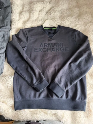 Mörkblå sweatshirt från Armani Exchange - Snygg mörkblå sweatshirt från Armani Exchange med broderad logga framtill. Tröjan har rund halsringning med V-detalj, långa ärmar och ribbade muddar. Perfekt för en stilren och avslappnad look.