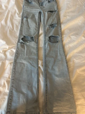 Ljusblå slitna bootcut jeans - Ljusblå bootcut jeans med flera stora och små slitningar. Slitna längst nere vid slutet av benen. Och även några fläckar längst ner vid ena benet som tyvärr inte går bort i tvätten 💛Har även tagit bort det rosa broderiet på bakfickorna.