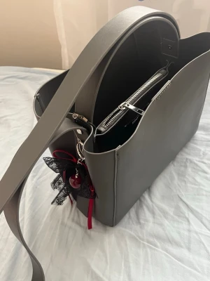 Grå väska - Grå väska från Gina tricot i nyskick. Slutsåld. Bag charm medföljer om man önskar det. 