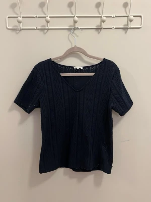 Mörkblå ribbad topp med v-ringning - Snygg mörkblå topp med v-ringning och korta ärmar. Toppen har ett ribbat mönster som ger en extra touch och är lätt att matcha till olika outfits. Perfekt för dig som gillar en enkel men stilren look.