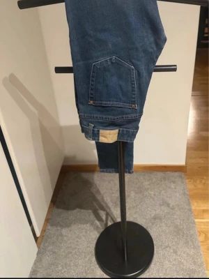 Mörkblå skinny jeans med hög midja - Snygga mörkblå skinny jeans med hög midja och klassiskar fem fickor. Jeansen har en enkel design med gylf och knapp framtill samt detaljer i kopparfärg. Perfekta för en trendig och avslappnad look.