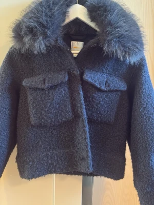 gina kappa med päls krage  - Snygg mörk blå pälsjacka med fluffig, bred fuskpälskrage och två stora fickor framtill. Jackan har en boxig passform och stängs med knappar. Perfekt för kalla vinterdagar när du vill vara både varm och trendig. passar xs 