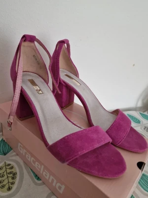 Rosa mocka-pumps från Metro. - Snygga rosa pumps i mockaimitation från Graceland med bred klack och öppen tå. Skorna har en smal rem runt ankeln med spänne och en enkel design som känns både trendig och stilren. Perfekta för dig som vill ha ett statement-plagg till din outfit. Köpt utomlands. Storlek 40, perfekt skick