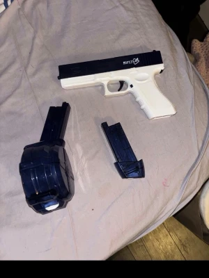 Elektrisk vatten pistol - Säljer en leksakspistol i vit och svart plast med två olika magasin, varav ett är ett större trummagasin. Pistolen har detaljerad design och passar för lek eller samlarhyllan. Märke Battle Electric Water gun