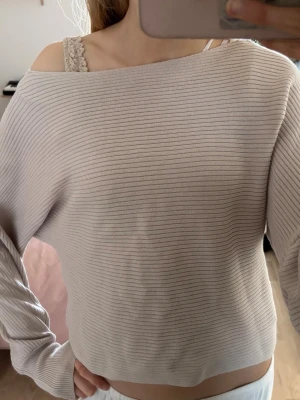 Beige ribbstickad off shoulder-tröja - Säljer en beige ribbstickad tröja med off shoulder-design och avslappnad passform. Tröjan har långa ärmar och bred ribbstruktur som ger en stilren look. Perfekt för dig som gillar en enkel men trendig stil. Nästan aldrig använd💕