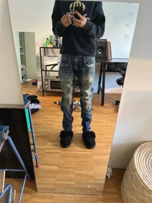 Blåa jeans från G-Star Raw - Säljer ett par blåa jeans från billionaire boys club med slitna detaljer och en stor broderad logga på bakfickan. Jeansen har normal passform och klassisk femficksdesign. Perfekta för dig som gillar streetwear och vill sticka ut lite extra.