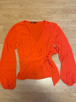 Orange omlottblus med knytband - Orange omlottblus från Gina Tricot med knytband i midjan. Strl 34