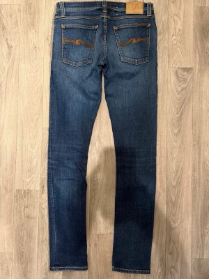 Nudie Jeans Tight Long John Jeans Mörkblå W29/L34 - Skinny Fit - Nudie Tight Long John mörkblå jeans med tight skinny fit och stretchig passform som sitter snyggt på kroppen, storlek W29/L34, midja 39 cm, ytterbenslängd 107 cm, benöppning 15 cm, modellen är 185cm & väger 65kg, i fint skick.