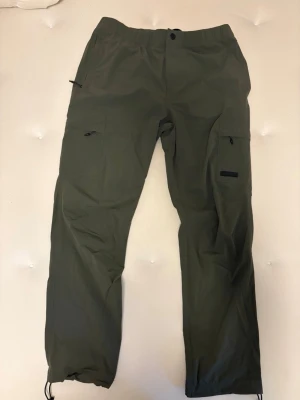 Militärgröna cargobyxor - Snygga militärgröna cargobyxor från H&M i regular fit. Byxorna har flera praktiska fickor med dragkedja, elastisk midja och justerbara benslut. Tillverkade i en lätt och slitstark polyesterblandning – perfekta för en avslappnad och trendig stil.