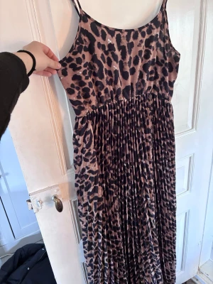 Leopardmönstrad långklänning från SHEIN - Snygg leopardmönstrad långklänning från SHEIN med tunna axelband och plisserad kjol. Klänningen har en rak, avslappnad passform och är i mjukt, lätt tyg. Perfekt för dig som vill sticka ut med ett djurmönster och trendig look. Passar snarare 40/42-M/L.