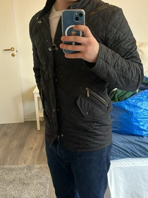 Svart quiltad jacka med dragkedja - Snygg svart quiltad jacka med dragkedja och knappar framtill. Jackan har två fickor med dragkedja och en klassisk krage. Perfekt för höst och vår, med långärmad design och stilren look.