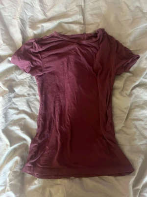 Vinröd kortärmad topp - En enkel vinröd t-shirt med korta ärmar och rund halsringning. Modellen är figurnära och tillverkad i mjukt bomullstyg, perfekt för en avslappnad och stilren look.