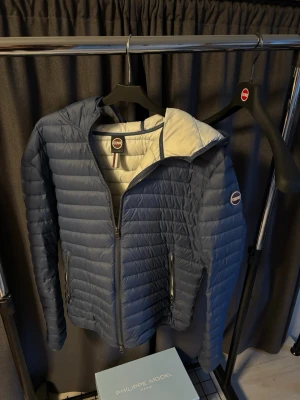 Blå pufferjacka från Colmar - Mörkblå lättviktsjacka från Colmar i quiltad design med smal passform. Jackan har genomgående dragkedja, två sidofickor med dragkedja och diskret logotyp på ärmen. Perfekt som vår eller som ett lätt lager under kallare dagar. Stilren och sportig modell med hög komfort. Storlek M| köpt för 2500kr|
