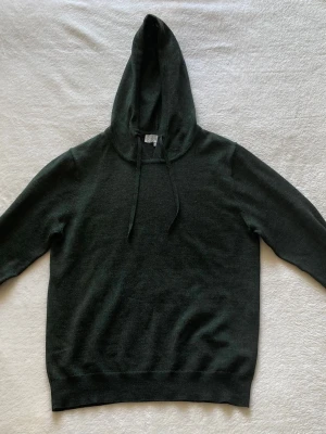 Mörkgrön hoodie - Säljer en mörkgrön stickad hoodie från Ahlquist Clothing i storlek S. Tillverkad i merinoull vilket gör den både mjuk, varm och bekväm. Tröjan är i superbra skick och har knappt använts. Stilren och premium känsla som passar perfekt till både vardag och finare outfits.