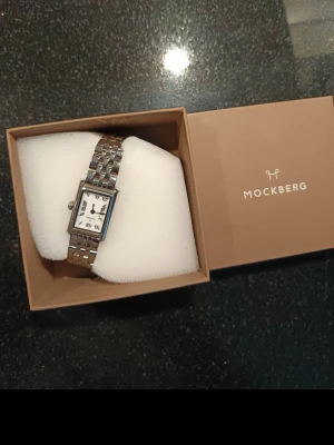 Mockberg silverfärgad rektangulär klocka - Stilren klocka från Mockberg med rektangulärt silverfärgat boett och länkarmband i metall. Vit urtavla med svarta romerska siffror och klassiska visare. Perfekt accessoar för en trendig look.