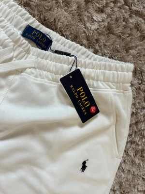 Vita shorts från Polo Ralph Lauren - Snygga vita shorts från Polo Ralph Lauren med klassisk logga broderad på benet. De har elastisk midja med snörning och två sidofickor. Perfekta för en avslappnad och stilren look. Materialet känns mjukt och bekvämt.