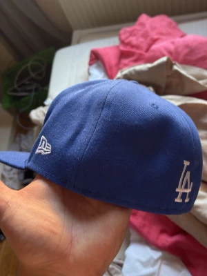 Blå LA Dodgers keps från New Era - Snygg blå keps från New Era med LA Dodgers-logga framtill och broderad World Series 1988-patch på sidan. Klassisk böjd skärm och broderade detaljer i vitt och lila. Perfekt för dig som gillar sportig streetstyle.