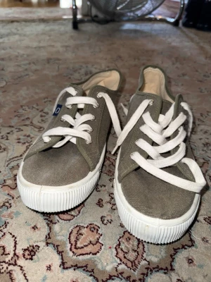 Olivgröna Superga canvas sneakers - Säljer ett par olivgröna Superga sneakers i canvas med vita gummisulor och vita snören. Klassisk låg modell med enkel design och diskret logga på sidan. Perfekta för en avslappnad och stilren look.