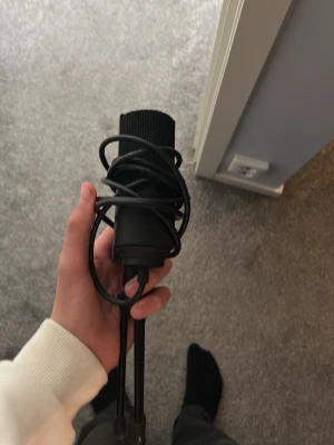 Svart USB-mikrofon med stativ - Säljer en svart USB-mikrofon med medföljande stativ och kabel. Mikrofonen har en cylindrisk form och är tillverkad i metall och plast. Perfekt för streaming, gaming eller poddinspelning.