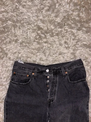 Gråa Levi’s jeans, W32, L31 - Snygga svarta jeans med raka ben och hög midja. Jeansen har klassisk femficksdesign och knäppning med flera silverfärgade knappar framtill. Perfekta till en avslappnad streetstil. Materialet är kraftig denim i bomull.